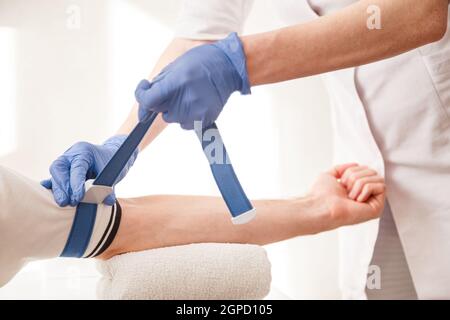 Nurse fissa il tourniquet medico sul braccio prima di prendere l'esame del sangue. Foto Stock