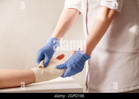 Il medico impone un bendaggio elastico al polso del paziente. Riabilitazione dopo la pioggia. Foto Stock