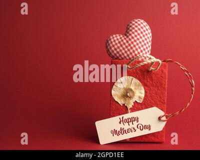 Piccola borsa di carta con una forma a cuore a scacchi su sfondo rosso, concetto di giorno Happy Mothers Foto Stock