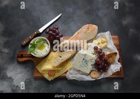 Piatto di formaggi con formaggi assortiti, uva, spuntini su sfondo scuro. Antipasto italiano e francese Foto Stock