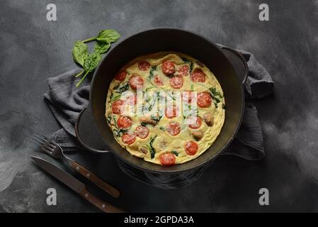 Frittata a base di uova, funghi, pomodori ciliegini e spinaci serviti in padella. Cucina italiana. Foto Stock