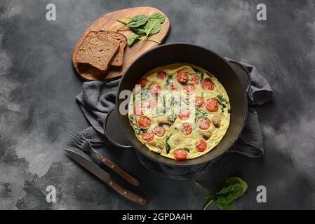 Frittata a base di uova, funghi, pomodori ciliegini e spinaci serviti in padella. Cucina italiana. Foto Stock