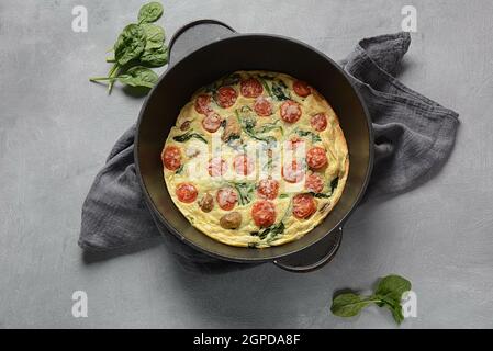 Frittata a base di uova, funghi, pomodori ciliegini e spinaci serviti in padella. Cucina italiana. Foto Stock