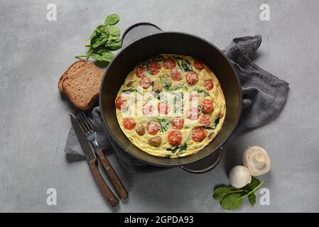 Frittata a base di uova, funghi, pomodori ciliegini e spinaci serviti in padella. Cucina italiana. Foto Stock