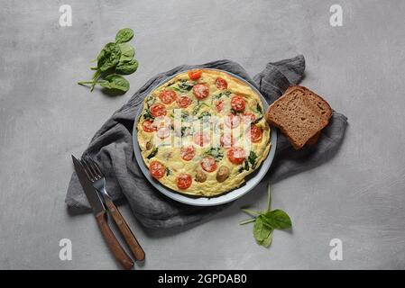 Frittata a base di uova, funghi, pomodori ciliegini e spinaci serviti su un piatto. Cucina italiana. Foto Stock