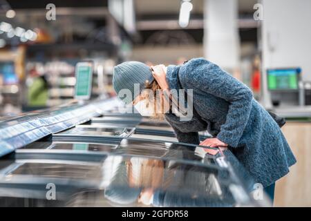 donna nel negozio sceglie il cibo dal freezer Foto Stock