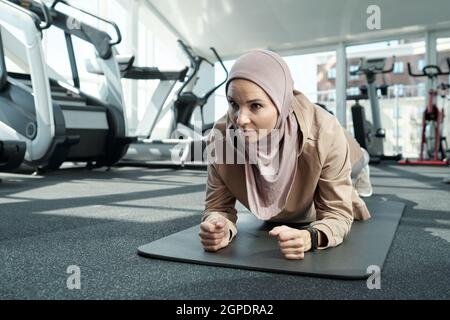Ritratto orizzontale medio in primo piano di una giovane donna musulmana forte adulto che indossa hijab facendo esercizio con asse a gomito in palestra Foto Stock