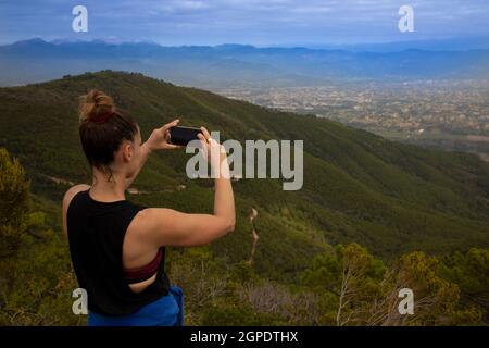 giovane atletica in cima alla montagna che scatta foto del panorama con il suo cellulare Foto Stock