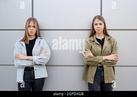 Due simpatiche ragazze bionda adolescenti in jeans neri e giacche incrociano le braccia al petto Foto Stock