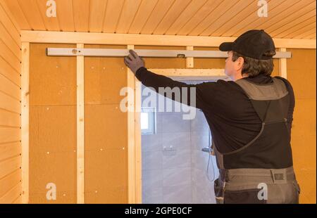 Costruzione di sauna, rifinitura. L'uomo sta avvitando una panca di legno al muro. Foto Stock