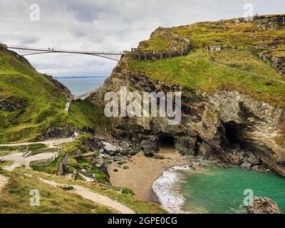 Ponte pedonale Tintagel con la Grotta di Merlin e la Cove Tintagel in primo piano. Foto Stock