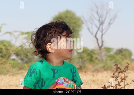 Primo piano vista profilo ritratto Un bambino giovane maschio di una famiglia di origine indiana che coltiva in piedi sul campo e guardando via con indossare t-shi verde Foto Stock