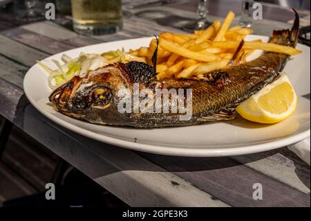 Pesce cotto a tavola. Orata di mare alla griglia con patatine fritte e limone al ristorante. Foto Stock