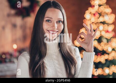 Ritratto di foto donna sorridente in maglia maglione mostrando un gesto OK vicino ornato albero di Natale Foto Stock