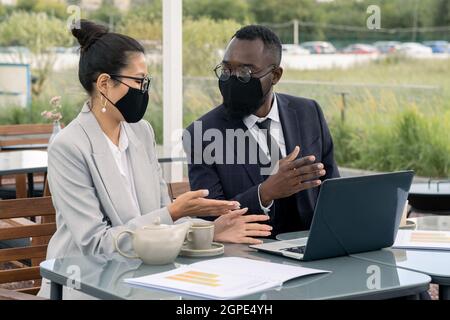Due giovani broker discutono di materiali per la presentazione durante una riunione all'aperto Foto Stock