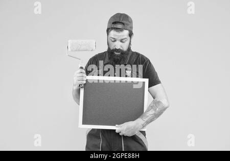 Penso che posso aiutarlo. Il caposquadra annuncia il servizio di parete che affronta. L'uomo con lo spazio di copia del bordo. hipster maturo usa l'attrezzo del rullo di vernice per la pittura Foto Stock