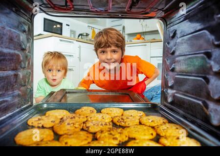 Due ragazzi aprono la porta del forno e guardano i biscotti freschi Foto Stock