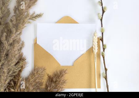 Mockup di carte minimalistico con fiore di canna, busta artigianale, fiore, piatto, vista dall'alto carta bianca bianca bianca bianca e busta per spazio di copia per te Foto Stock