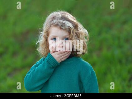 Sorpreso bambino biondo con gli occhi blu che copre la sua bocca Foto Stock