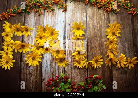Concetto autunnale, parola 'autumna' con fiori gialli su sfondo di legno decorato con bacche Foto Stock