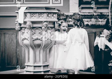 Una foto in scala di grigi di ragazze carine caucasiche in abiti bianchi che giocano all'angolo della stanza Foto Stock