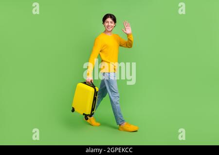 Corpo a tutta lunghezza foto uomo che mantiene la valigia ondeggiante mano in aeroporto isolato pastello colore verde sfondo Foto Stock