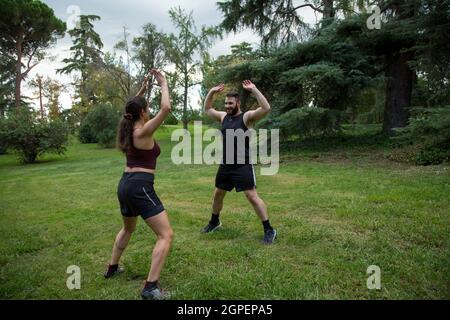 giovane felice uomo caucasico e donna coppia praticare burpee in giardino Foto Stock