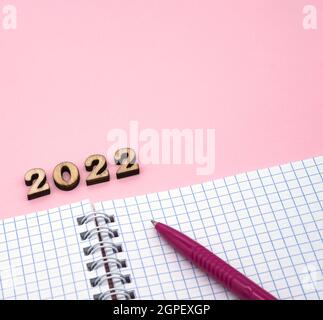 Numeri in legno 2022. Blocco note su una molla. Blocco note e penna su rosa. Penna rosa. Fogli a spirale a scacchi. Foto Stock