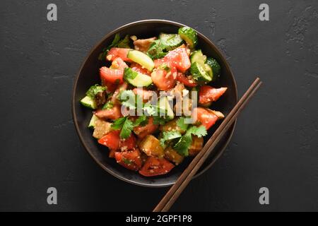 Melanzane speziate e croccanti cinesi con cetriolo, aglio, pomodori, foglie di coriandolo fresco in salsa di ostriche e aceto nero su sfondo nero. Vista da Foto Stock