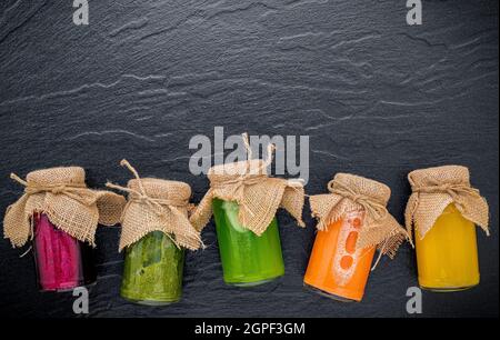Colorati Frullati salutari e di succhi di frutta in bottiglie in pietra scura con sfondo spazio copia. Foto Stock
