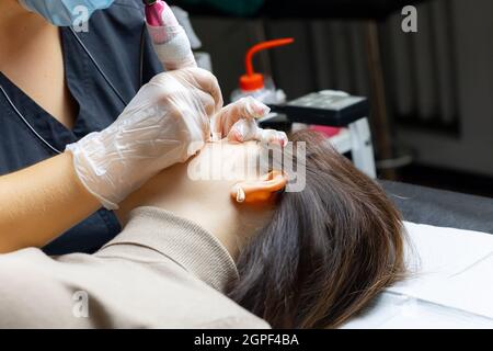 il padrone del trucco permanente siede alla testa del letto ed esegue la procedura di tatuaggio palpebrale Foto Stock