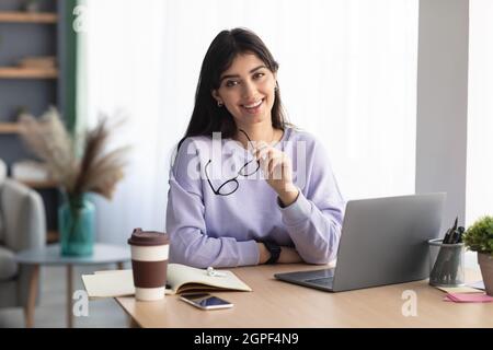 Ritratto di giovane donna sorridente seduto alla scrivania Foto Stock