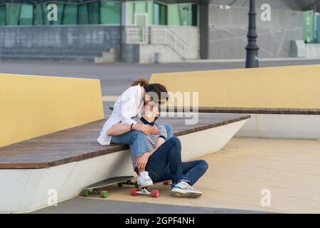 Un paio di pattinatori che si baciano si siedono a bordo lungo insieme all'aperto nello spazio urbano. Gioventù, romanticismo e amore Foto Stock