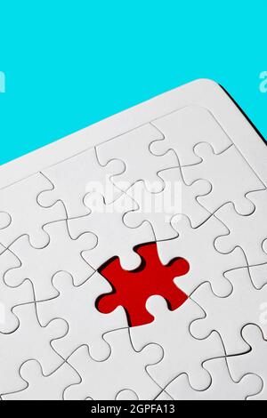 primo piano di un buco rosso in un puzzle bianco vuoto manca un pezzo su sfondo blu Foto Stock