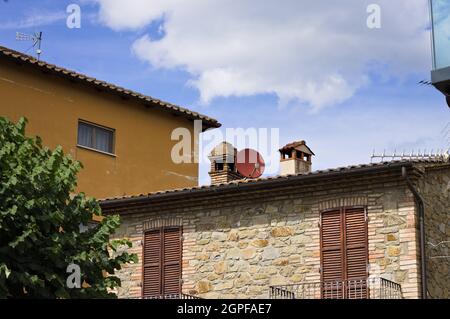 Un piatto satellite rosso posto tra due camini sul tetto di una casa in pietra (Umbria, Italia, Europa) Foto Stock