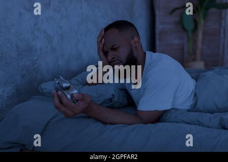 Uomo nero che soffre di insonnia guardando l'orologio Foto Stock
