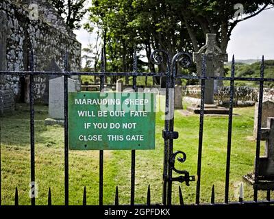 Divertente cartello all'ingresso del cortile della chiesa di Kildalton con Kildalton Cross sullo sfondo Foto Stock