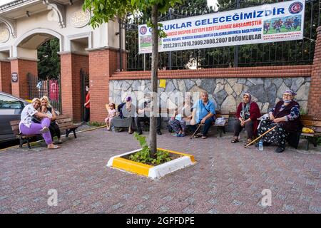 Beyoglu, Istanbul, Turchia - 06.27.2021: Un sacco di felice turco Romany Gypsy cittadini e la famiglia seduti su banchi pubblici e guardando fotocamera e po Foto Stock