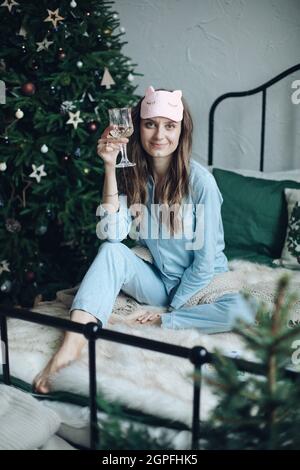 Donna sorridente che indossa pigiami e beve champagne a Natale Foto Stock