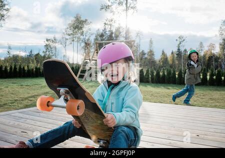 ragazza sedette su uno skateboard ridendo con suo fratello che gioca a casa Foto Stock