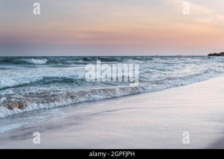 paesaggio di onde di mare che si infrangono sulla spiaggia contro il tramonto rosa Foto Stock