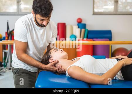 Mani dell'uomo che fanno il collo di articolazione manuale che si allunga e che danno un massaggio del collo ad una giovane donna caucasica Foto Stock