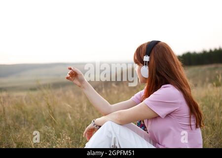 La giovane donna rossa nelle cuffie ascolta la musica in natura Foto Stock