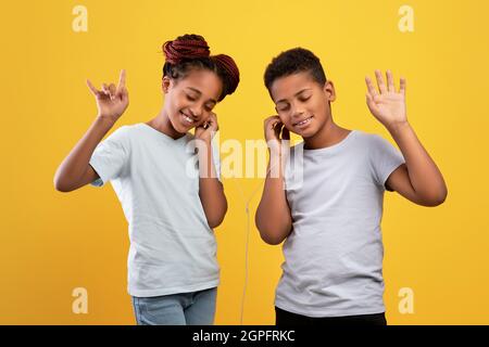 Gioiosi fratelli afro-americani con auricolari che ascoltano musica Foto Stock