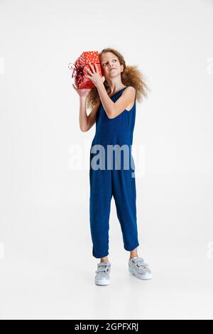 Un felice carino caucasico ragazza piccola mannatura blu vestito in piedi con enorme regalo, scatola per le vacanze isolato su sfondo grigio studio con copyspace per l'annuncio Foto Stock