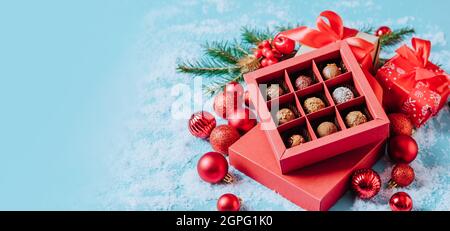 Cioccolatini in una scatola rossa festive tartufo al cioccolato fondente su sfondo natalizio con palline di Capodanno rami di abete. spazio copia mock up piatto. Foto Stock