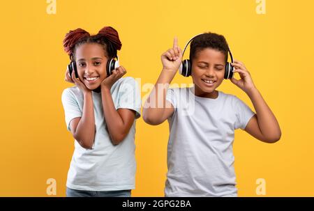 Emotivi fratelli neri con cuffie wireless che ascoltano musica Foto Stock