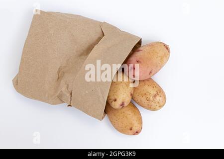 mucchio di patate fresche crude sono cosparse da un piccolo sacchetto di carta isolato su sfondo bianco, verdure crude, raccolta di patate rosse nuove, vista laterale Foto Stock