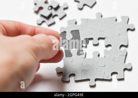 Foto di una persona che aggiunge l'ultimo pezzo di puzzle per adattarsi insieme su sfondo bianco Foto Stock