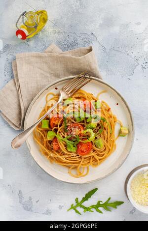 Spaghetti al pesto, avocado e pomodori in rustico piatto bianco. Concetto di cibo vegano crudo. Vista dall'alto. Foto Stock